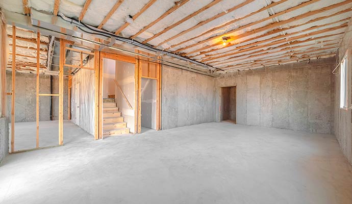 An unfinished basement showing concrete floors, wooden wall framing, and ceiling insulation near a staircase