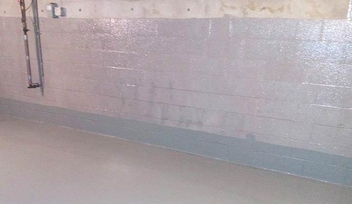 A basement interior with a glossy waterproof sealer applied to the concrete block walls and floor to prevent moisture intrusion
